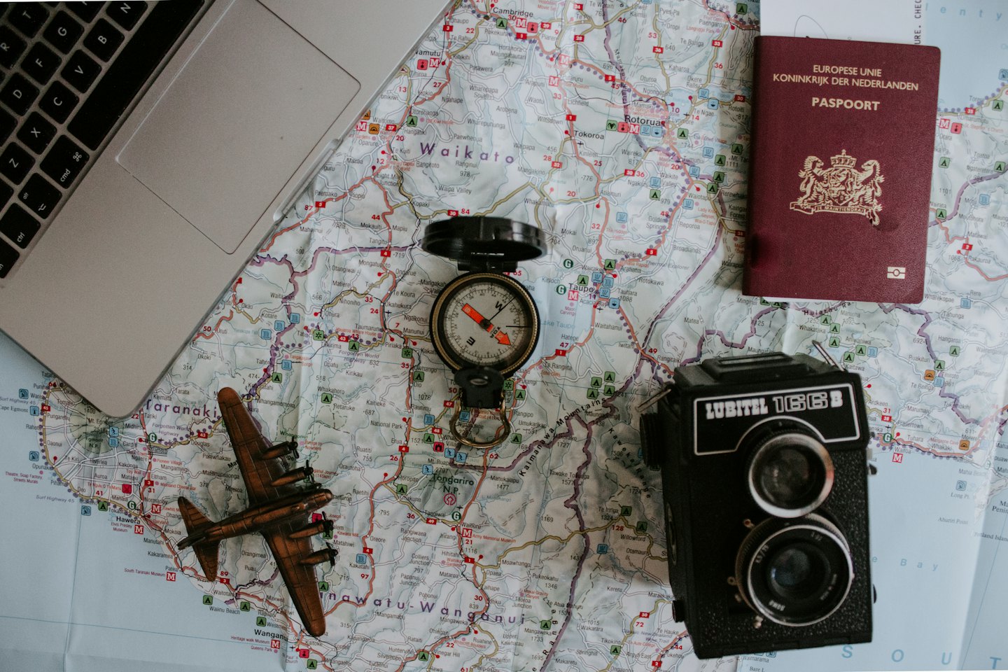 Przedmioty podróżne, w tym laptop, kompas, aparat i paszport na mapie.